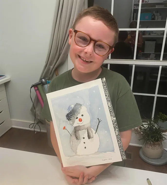 Smiling child holding snowman painting