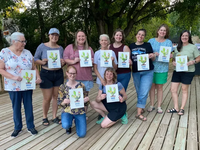 Smiling women holding cactus prints on deck