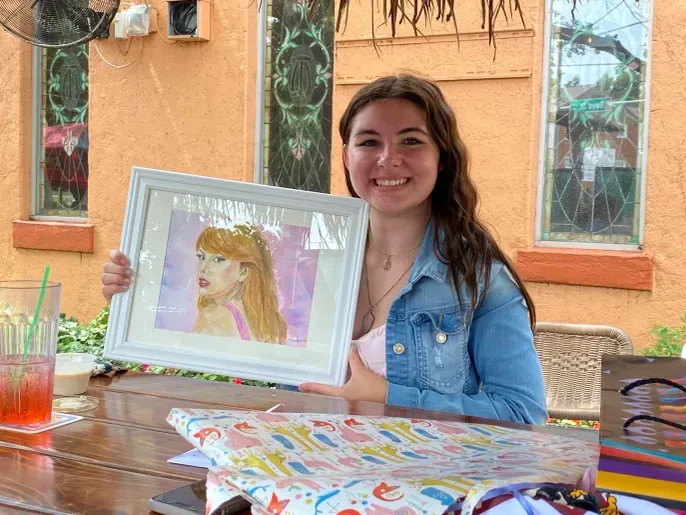 Smiling woman holding framed portrait artwork outdoors