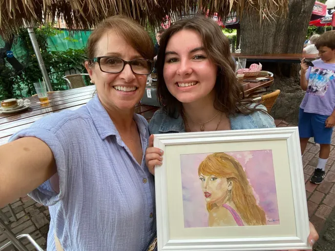 Two women smiling holding framed portrait painting