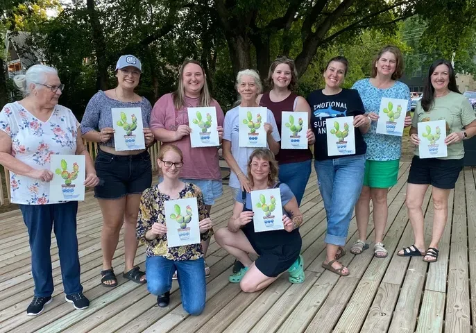 Smiling women holding cactus prints on deck