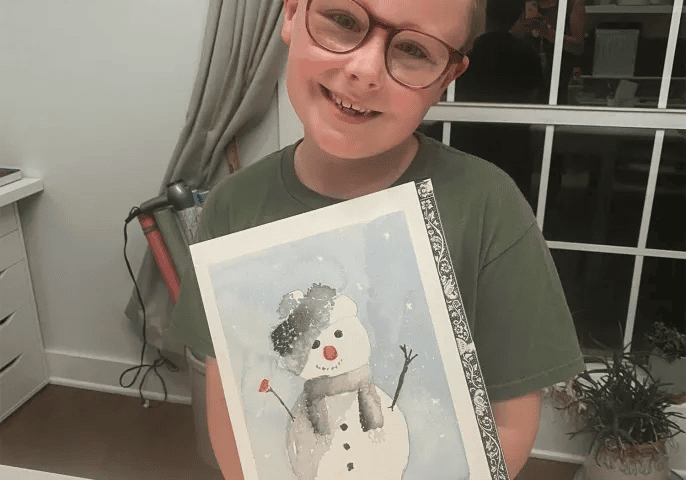 Smiling child holding snowman painting